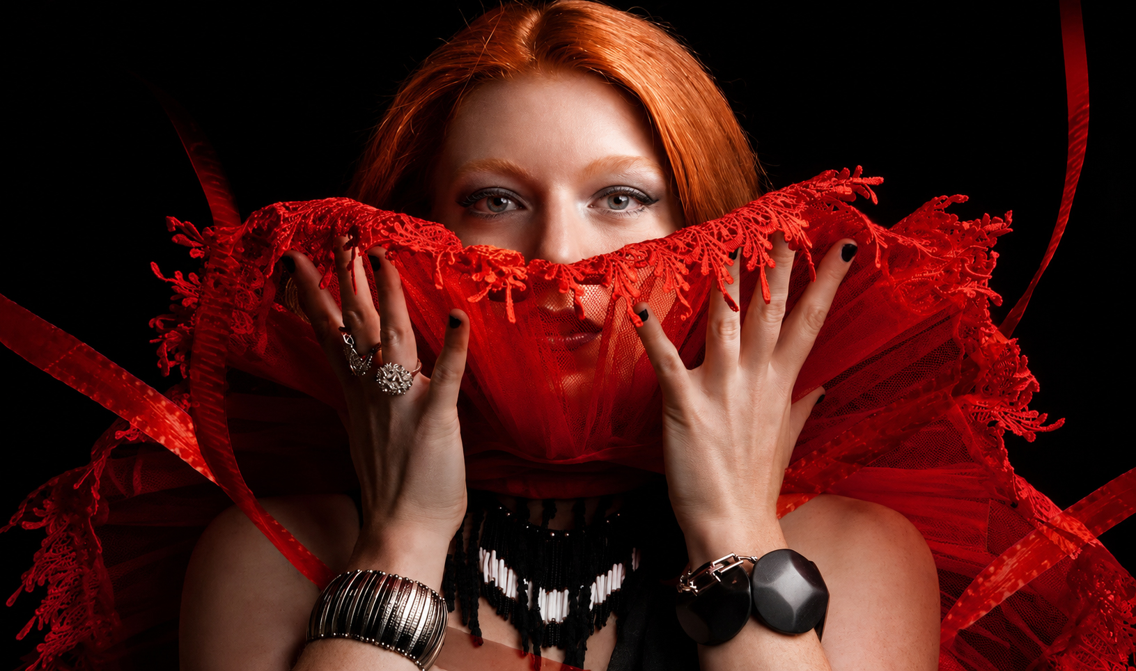 Red-haired portrait subject holding dramatic red lace fabric near her face
