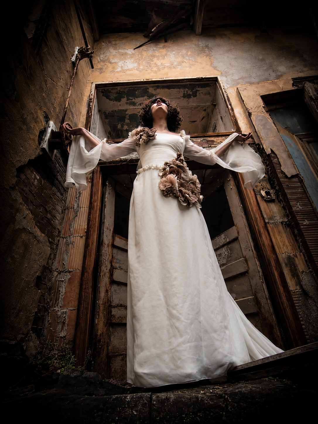 Woman in a white gown standing in a ruined doorway with arms outstretched