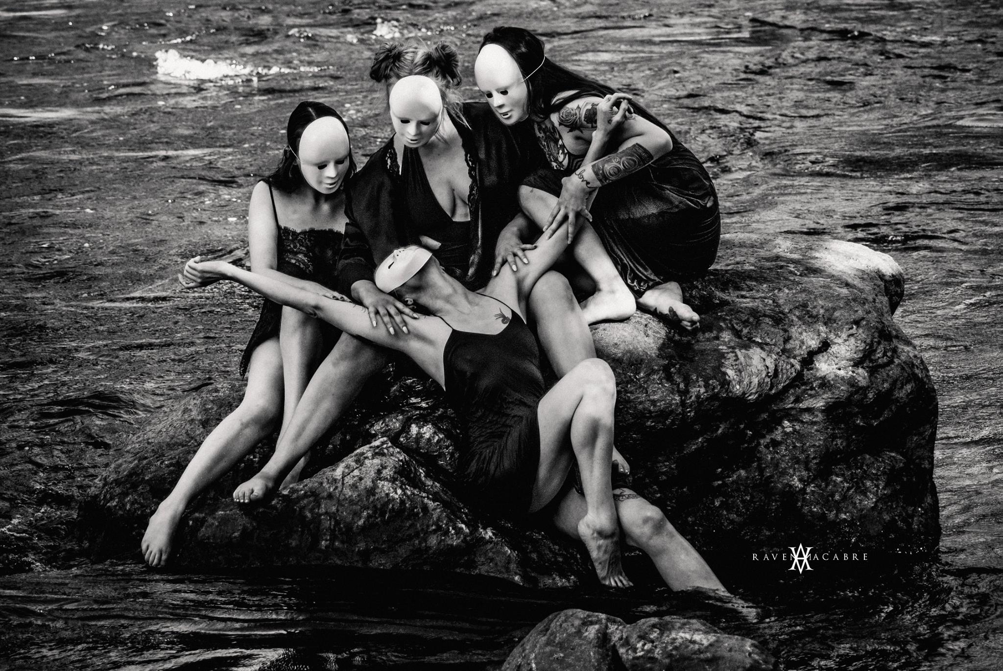 Masked figures posed together on rocks in moving water